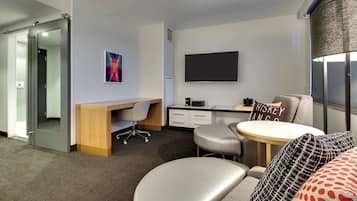 Una habitación de hotel moderna con escritorio, televisión de pantalla plana, zona de estar confortable y un ventanal amplio.