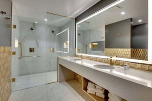 A modern bathroom with a glass-enclosed shower, dual sinks, and a large mirror.