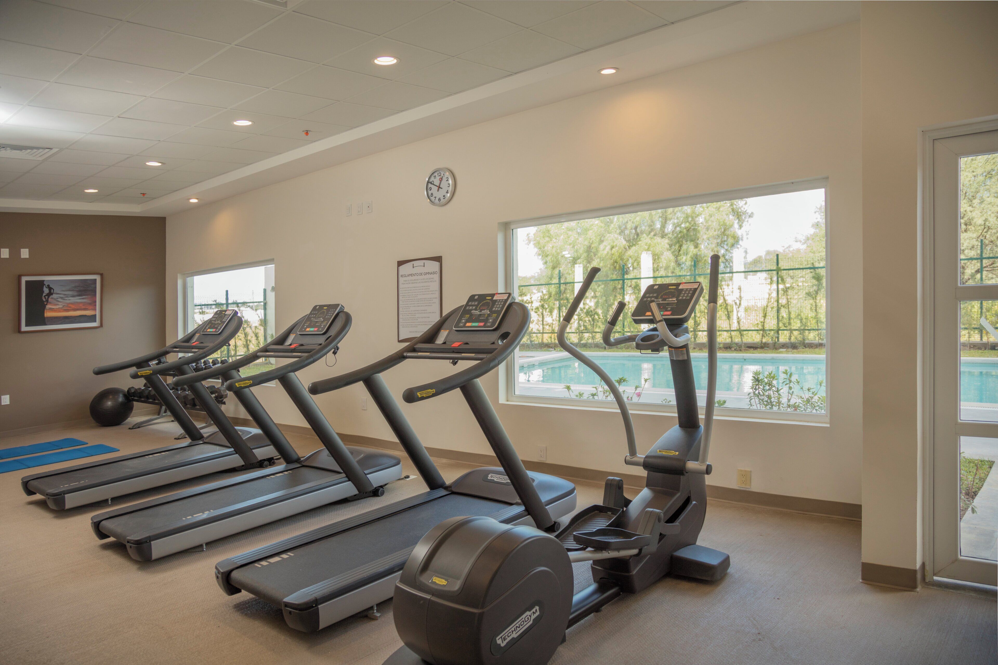 A gym with treadmills, ellipticals, and a pool view.