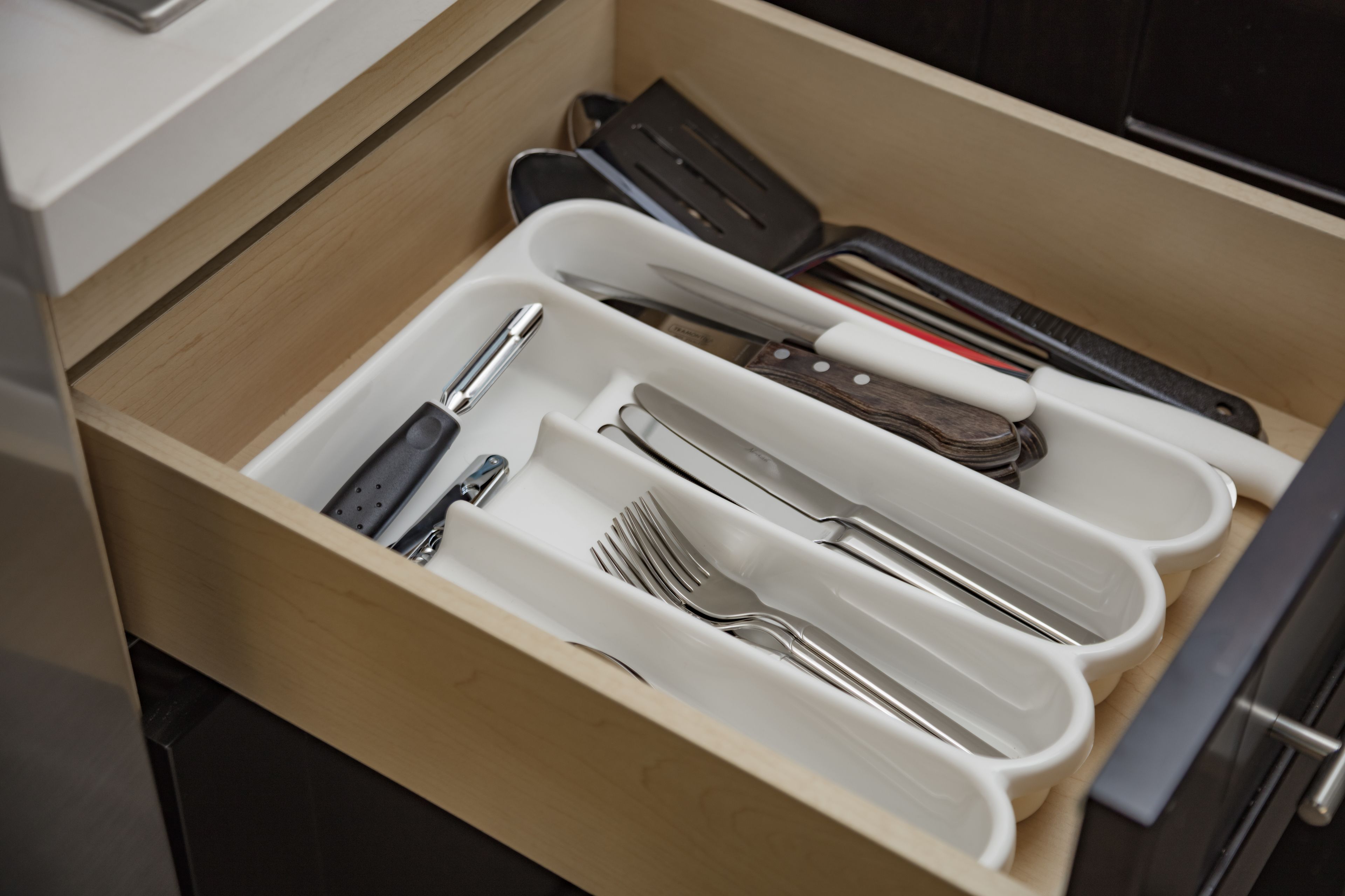 Un cajón con divisiones que contiene diversos utensilios de cocina, como cuchillos, tenedores y cucharas.