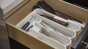Un cajón con divisiones que contiene diversos utensilios de cocina, como cuchillos, tenedores y cucharas.
