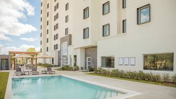 A hotel with a swimming pool, outdoor seating, and a covered patio area.