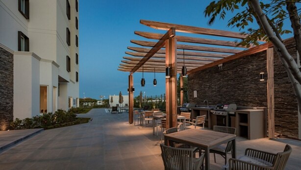 Un patio exterior con pérgola de madera, paredes de piedra y zona de barbacoa.