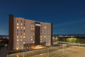 Un hotel de varios pisos con un llamativo letrero de 'Staybridge', un estacionamiento y vistas de la ciudad al fondo.