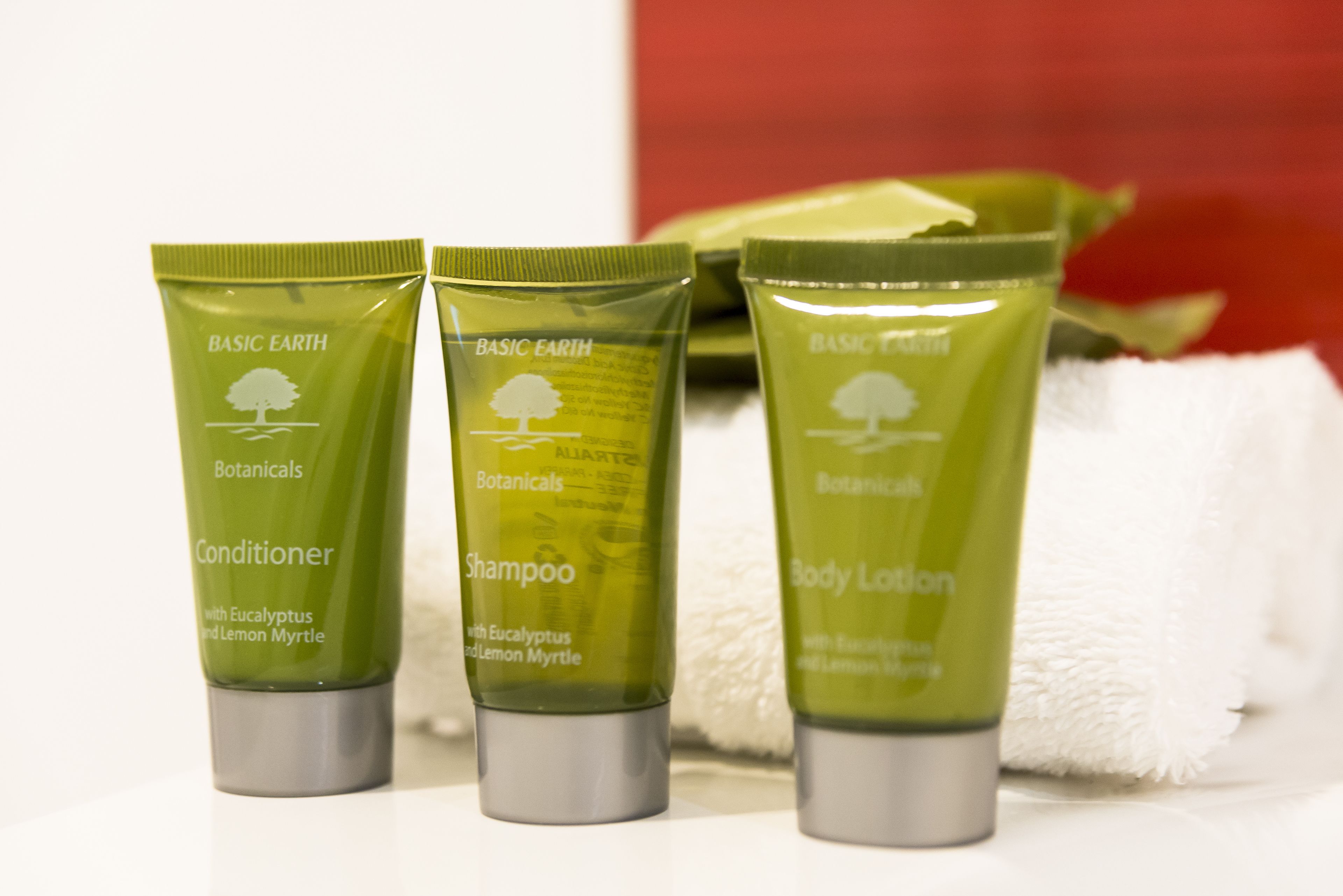Three green bottles of Basic Earth Botanicals products: conditioner, shampoo, and body lotion.