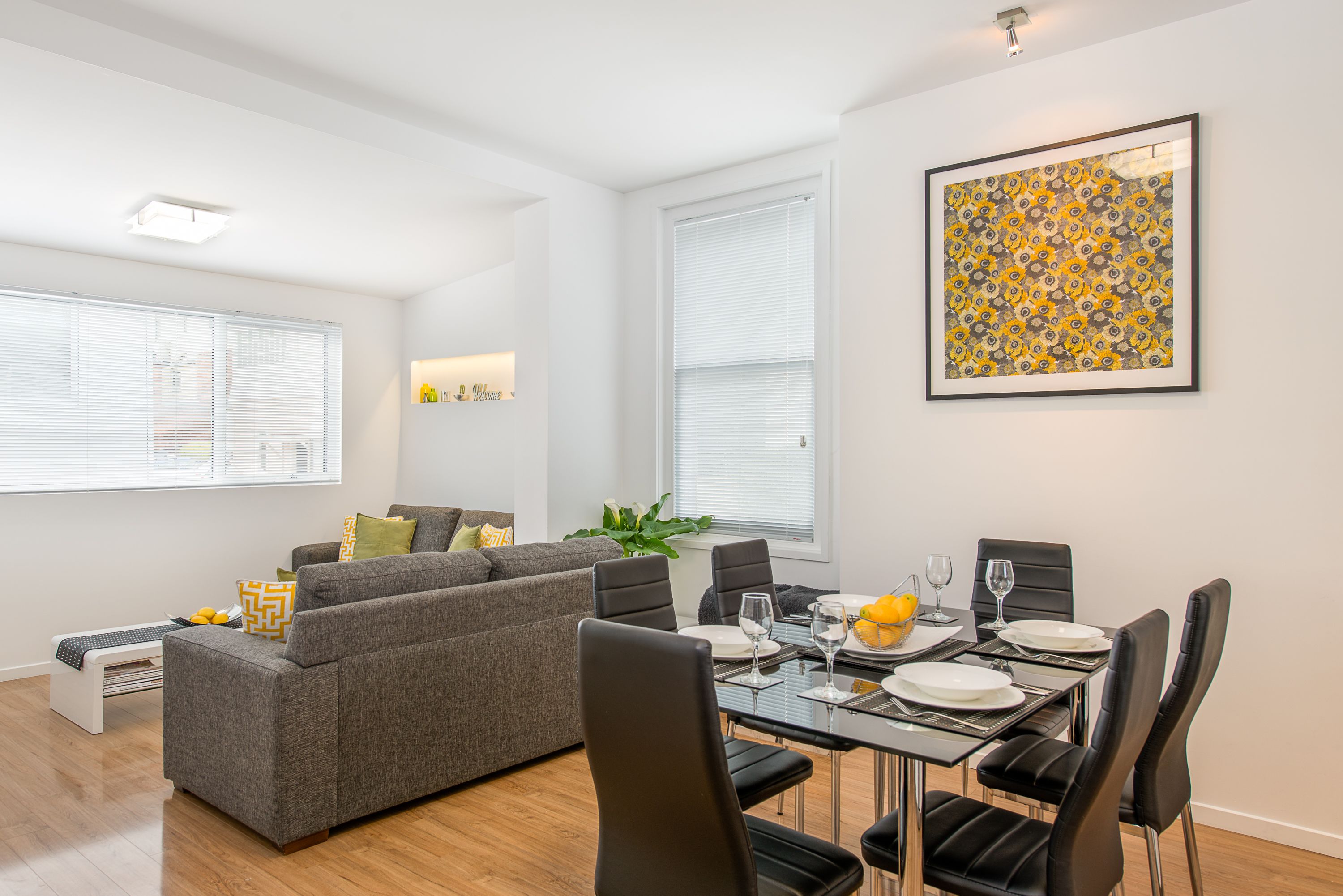Uma sala de estar moderna com área de jantar, apresentando um sofá cinza, cadeiras pretas e uma mesa de jantar posta para seis pessoas.