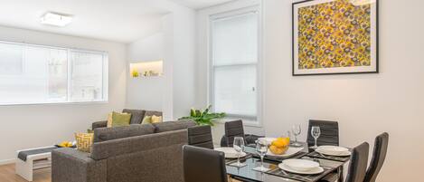 Uma sala de estar moderna com área de jantar, apresentando um sofá cinza, cadeiras pretas e uma mesa de jantar posta para seis pessoas.