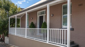 A two-story house with a covered porch, a front door, and a small front yard with two potted plants. - Hobart Cityscape (Hobart)