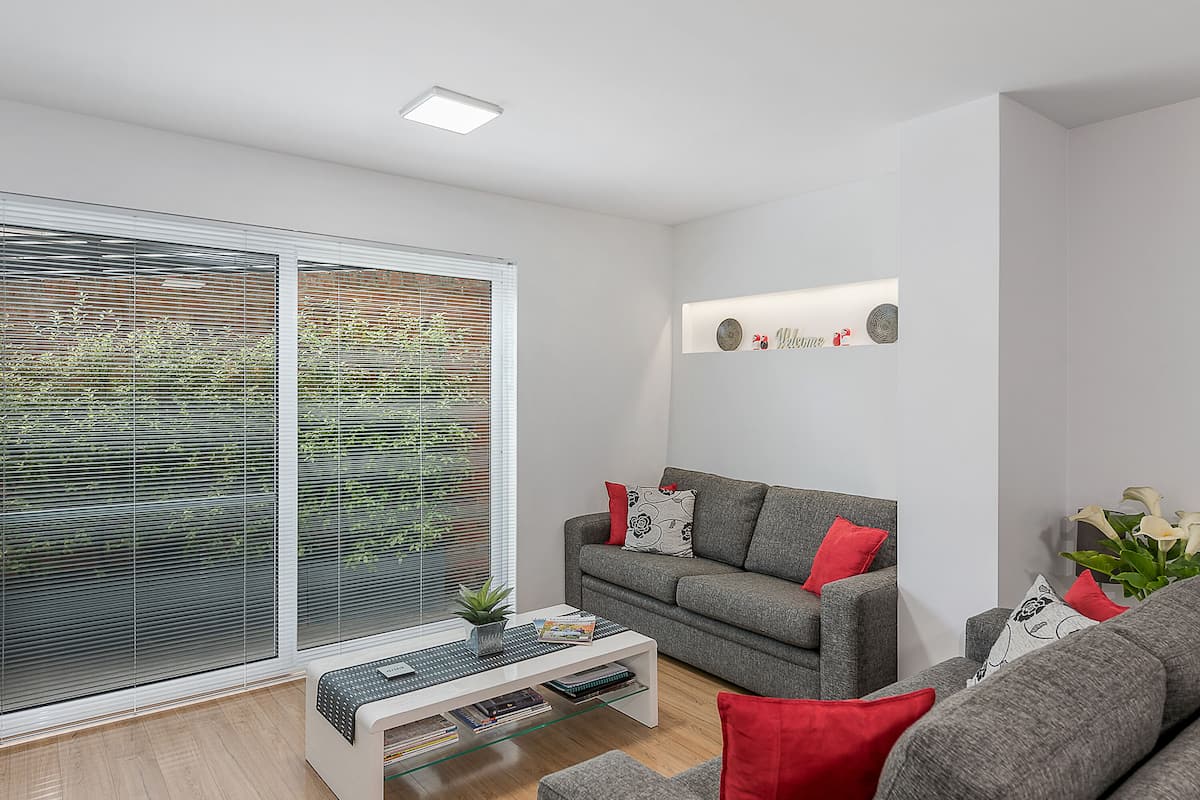 Una sala de estar moderna con un sofá gris, cojines rojos, una mesa de centro de cristal y una estantería.