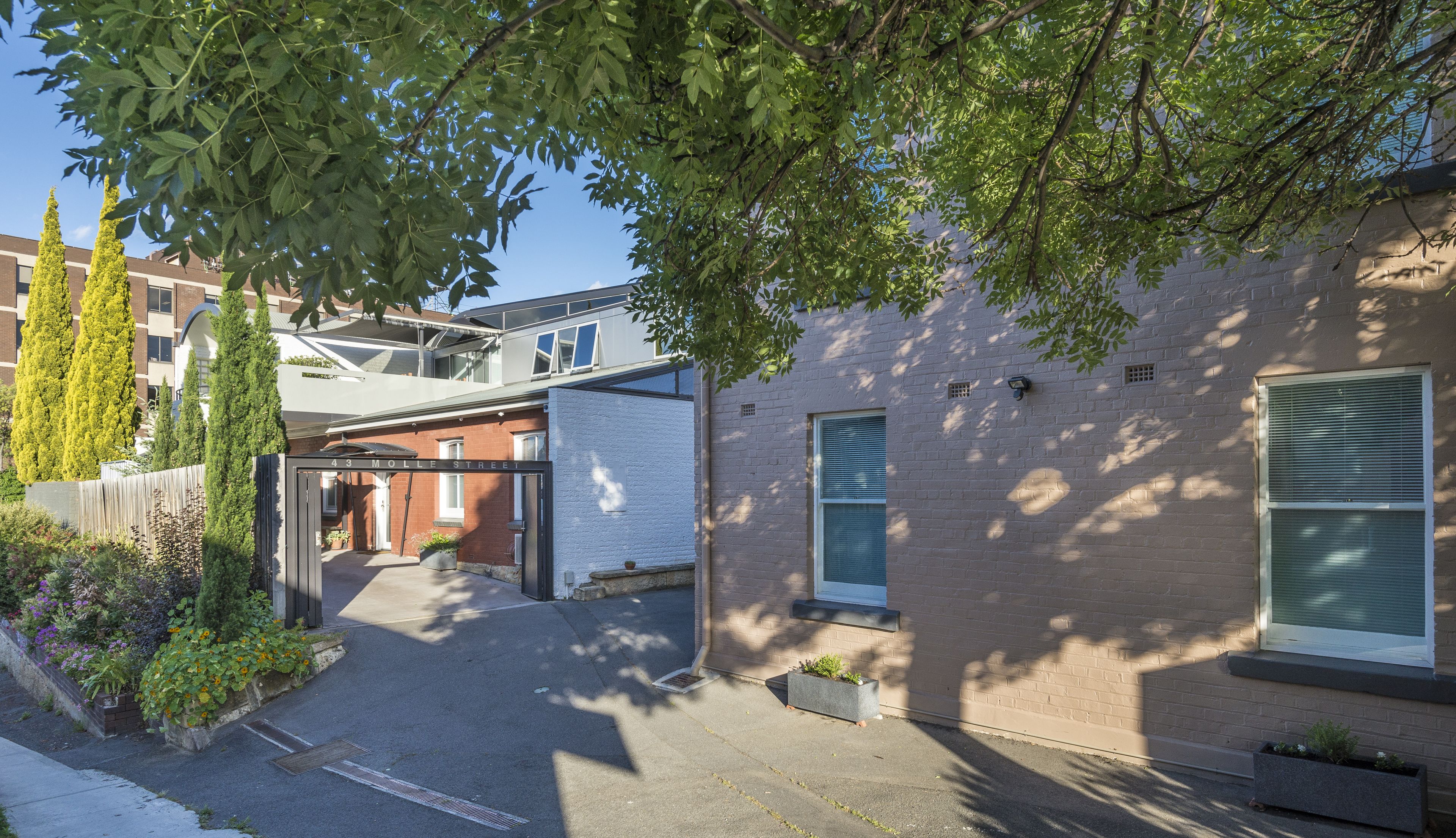 A residential building with a brick facade, a gated entrance, and a small garden area with potted plants.