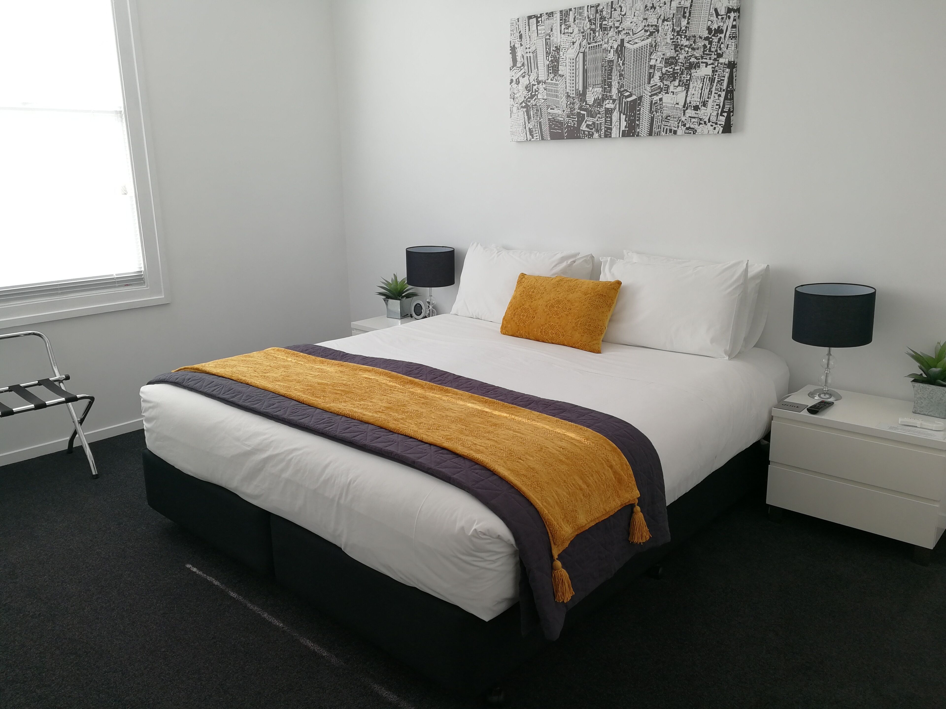 A modern bedroom with a bed, nightstands, a lamp, a plant, and a window.