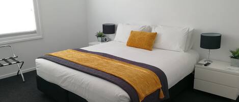 A modern bedroom with a bed, nightstands, a lamp, a plant, and a window.