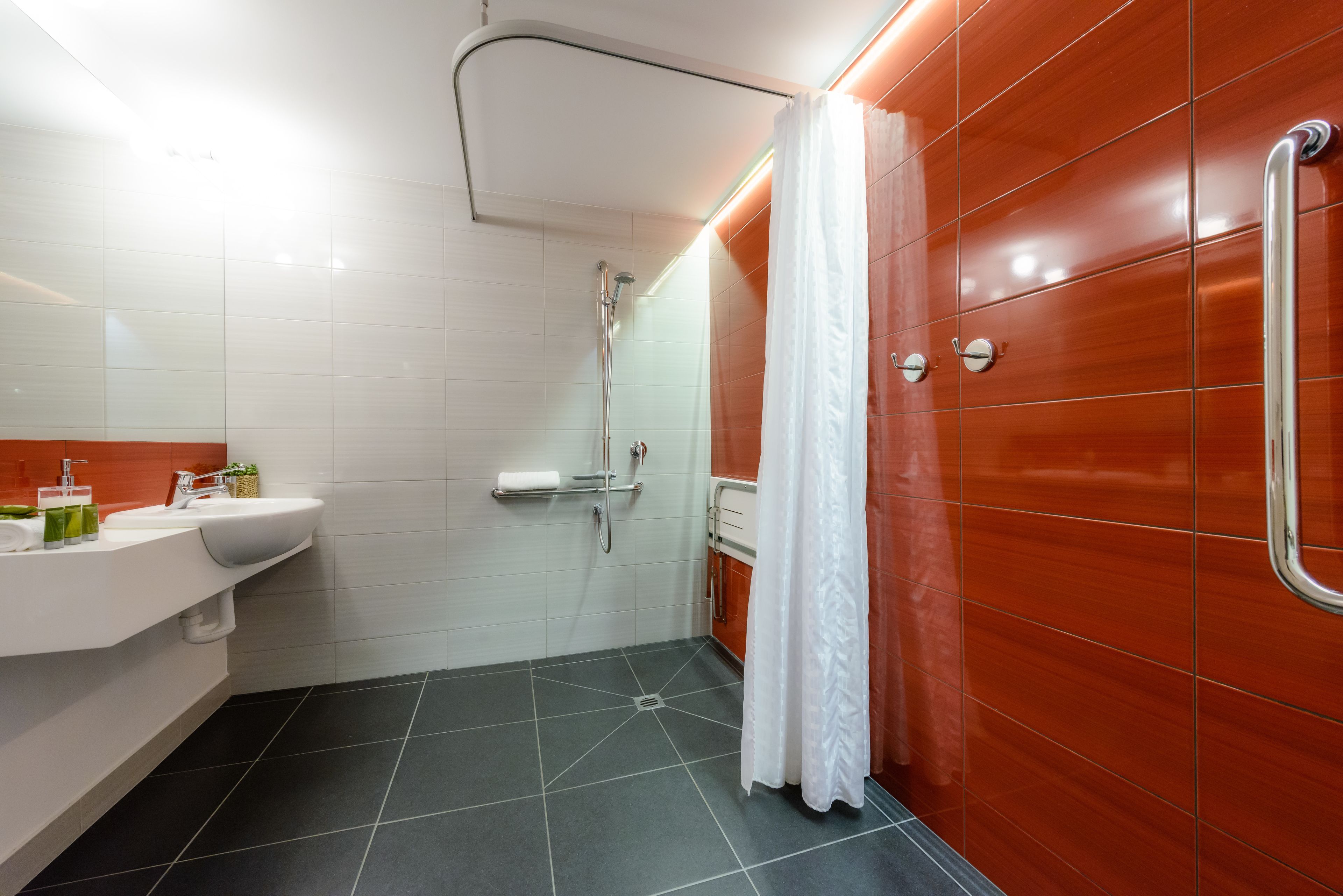 A modern bathroom with a white sink, a shower with a glass door, and a red tiled wall.