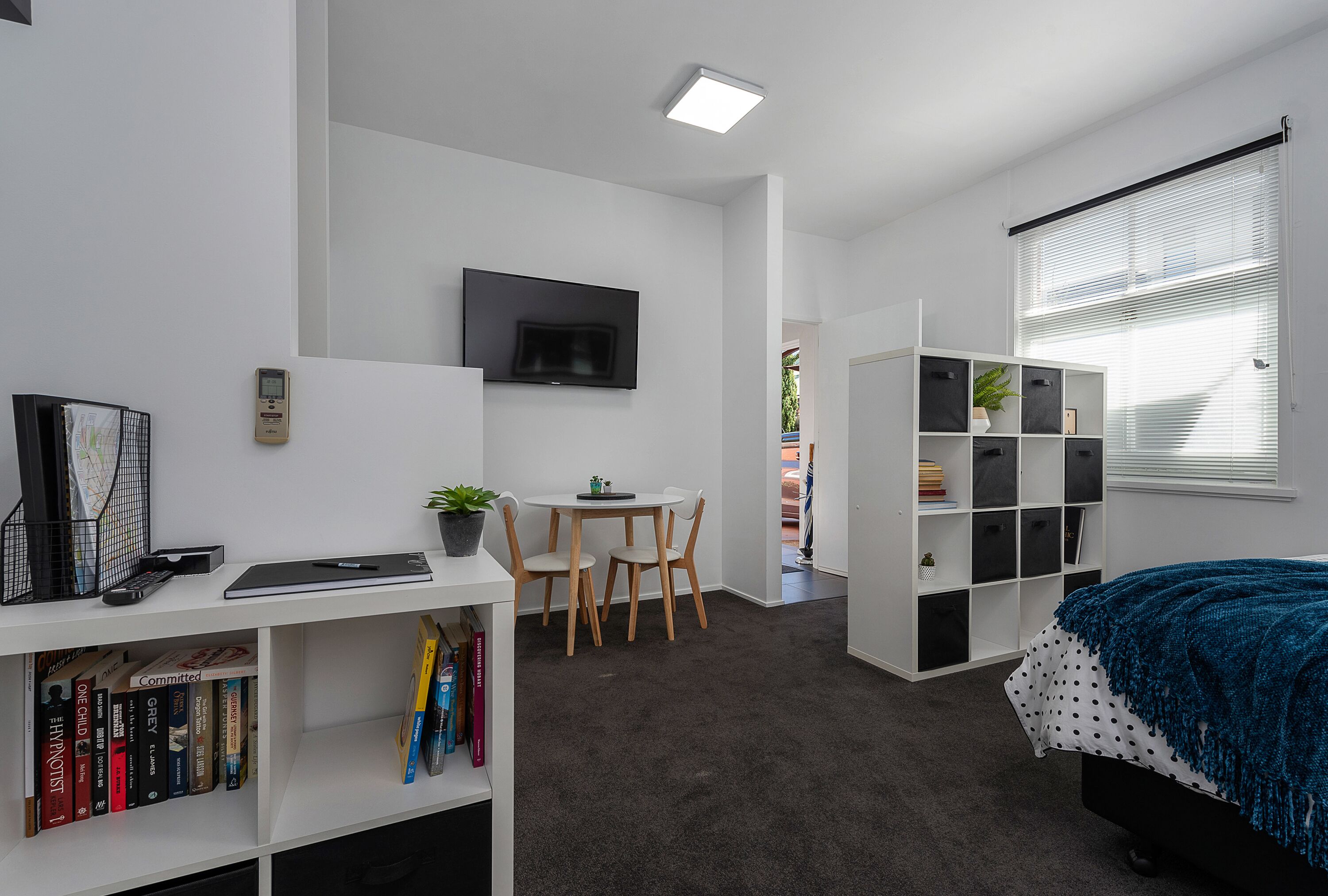 A modern, well-lit room with a desk, chair, bookshelf, and a bed with a polka dot blanket.