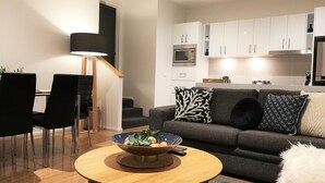 A modern living room with a grey sofa, black and white patterned pillows, a wooden coffee table with a bowl and remote control, and a dining area with black chairs and a lamp. - Hobart Cityscape (Hobart)