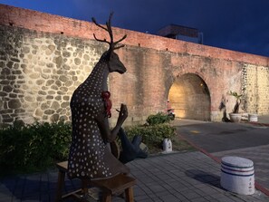 A sculpture of a deer with antlers and a bow, positioned on a bench in front of a stone wall with an arched passageway. - Bird house (Hengchun)