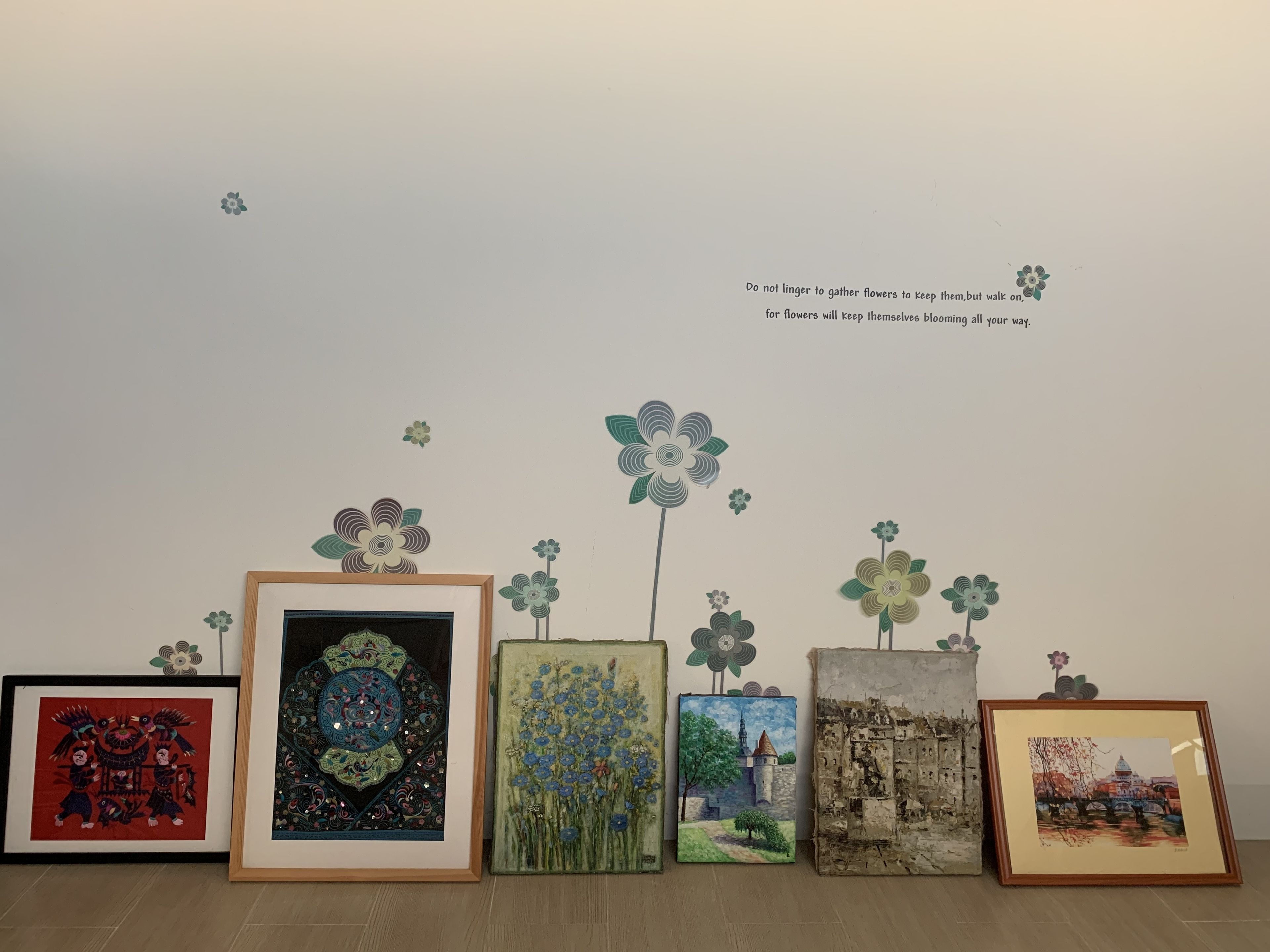 A gallery wall with various framed artworks, including a colorful tapestry, a painting of a castle, and a landscape.