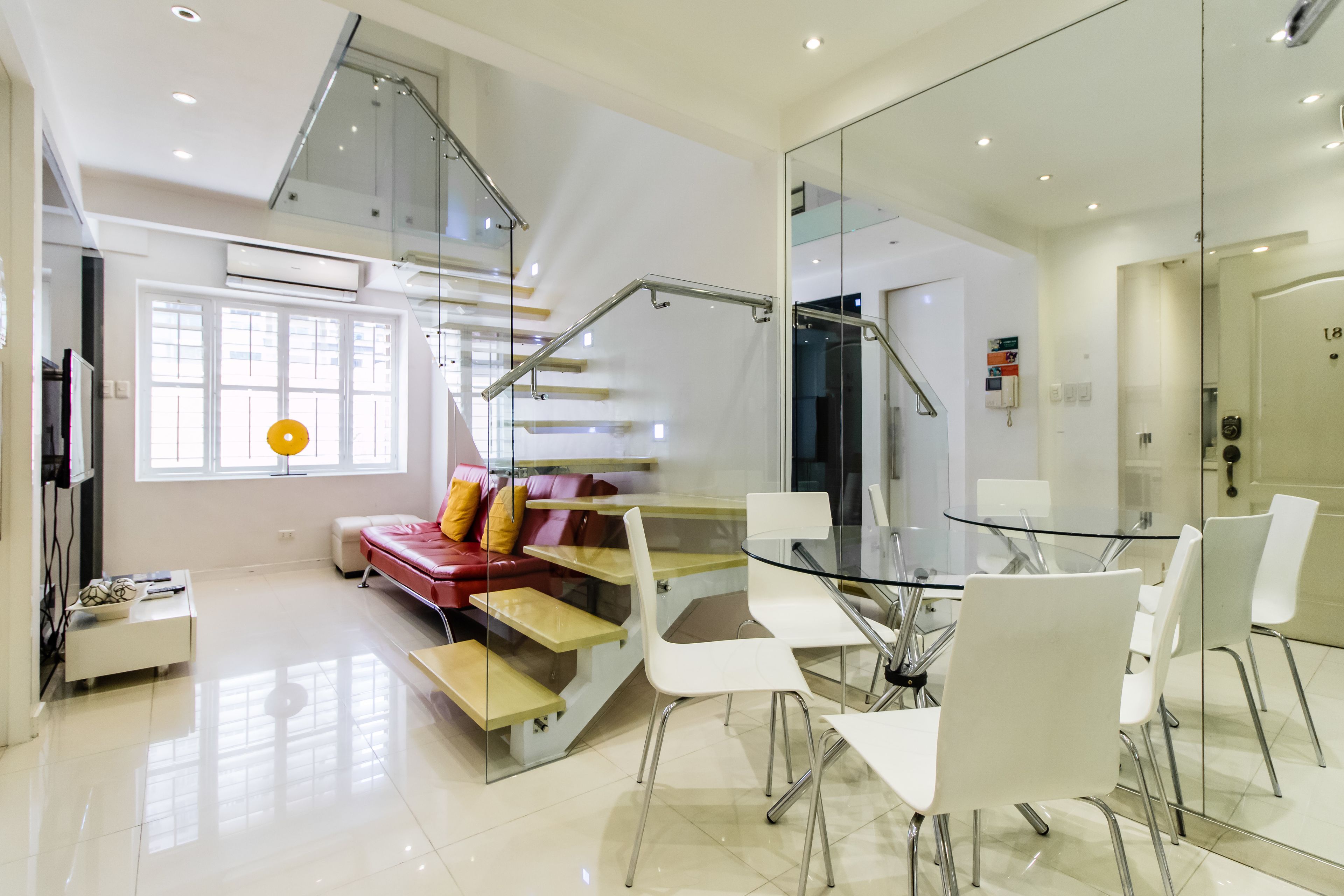 Ein modernes Interieur mit einer Glasstaircase, einem Essbereich mit weißen Stühlen und einem roten Sofa mit gelben Kissen.