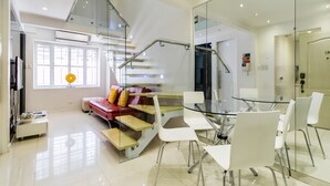 A modern interior with a glass staircase, a dining area with white chairs, and a red sofa with yellow cushions. - Alcoves Greenbelt Park Place Makati (Makati)