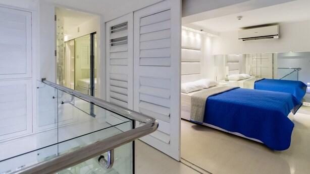 A modern hotel room with a glass balcony, a bed with blue bedding, and a large mirror reflecting the room. - Alcoves Greenbelt Park Place Makati (Makati)
