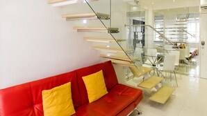 A modern interior with a red leather sofa, a glass staircase, and a dining area. - Alcoves Greenbelt Park Place Makati (Makati)