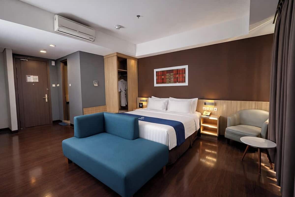 Quarto de hotel com cama, sofá azul, cadeira, mesinha e armário.