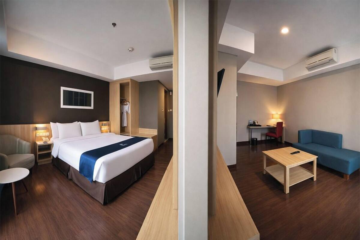 Quarto de hotel com cama, escrivaninha, cadeira, sofá e uma pequena mesa.
