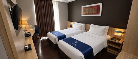 A hotel room with two beds, a TV, a desk, a chair, and a window with curtains.