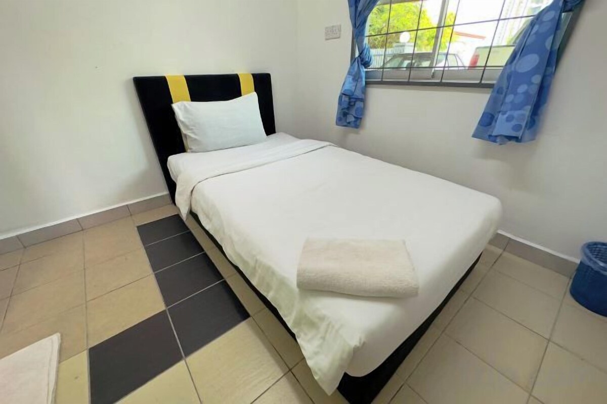A single bed with a white mattress and a black headboard, a window with blue curtains, and a tiled floor.