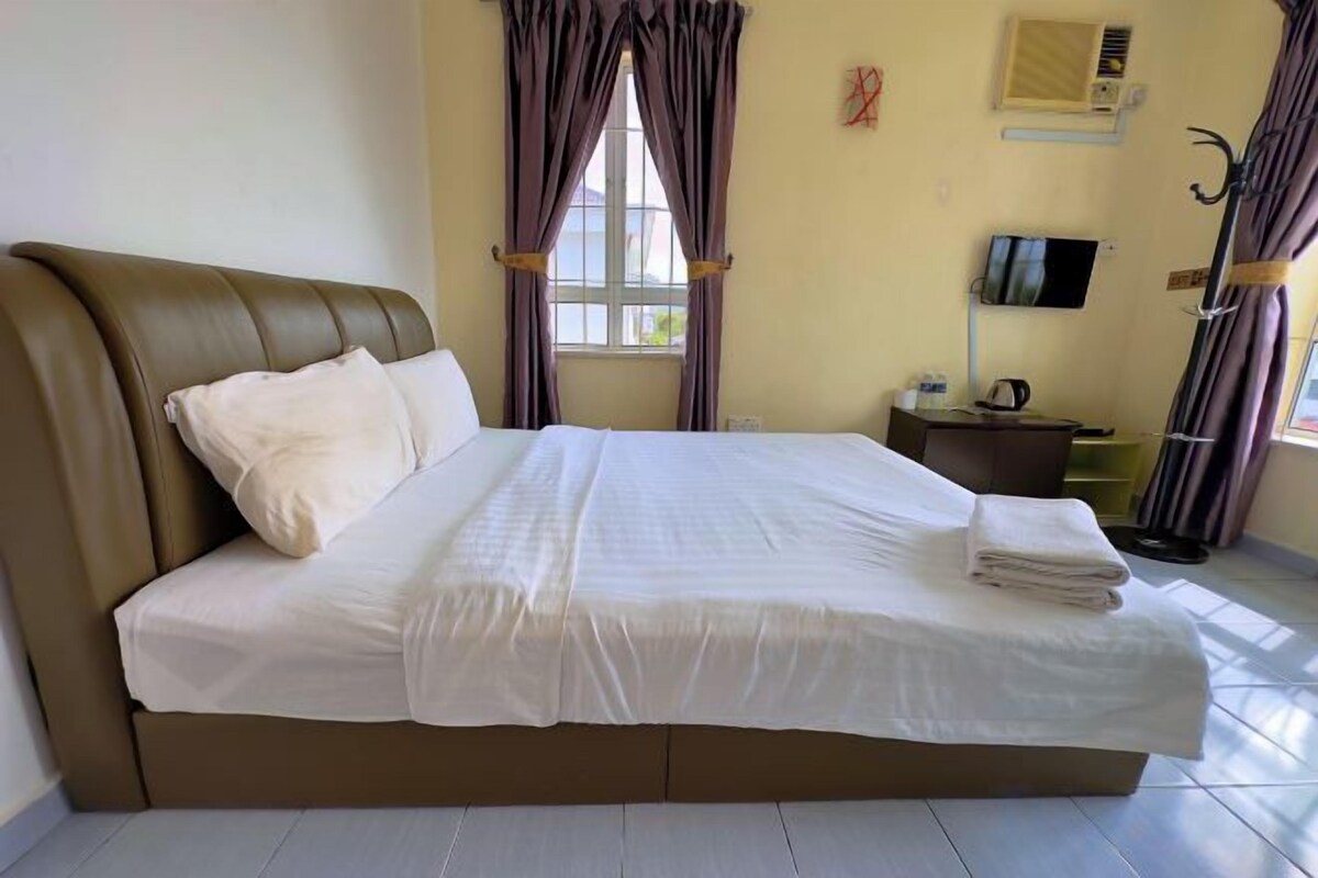 Une chambre d’hôtel avec un grand lit, un téléviseur à écran plat et une fenêtre avec des rideaux.