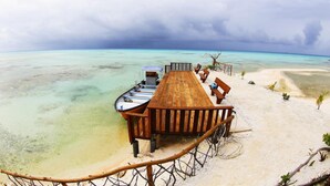 Bungalows über dem Wasser mit Holzterrasse, Liegestühlen und Blick auf das türkisblaue Meer und den klaren Himmel.