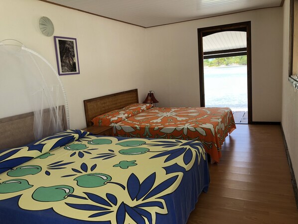 A room with two beds, a wooden floor, a window, and a door leading outside.