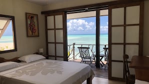Ein Hotelzimmer mit einem Bett, einem Gemälde und Blick auf den Ozean durch eine Schiebetür.