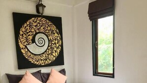 Een net opgemaakt bed met een wit laken en twee gevouwen handdoeken, een zwart-wit kunstwerk aan de muur, en een raam met uitzicht op groen.