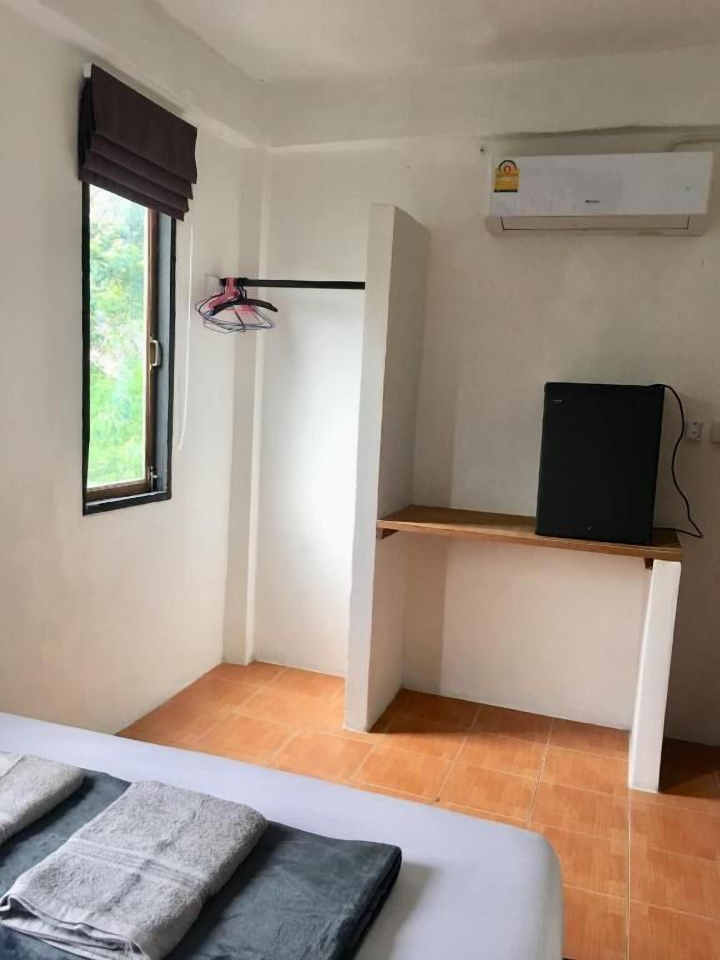A small, sparsely furnished room with a bed, a desk, a chair, and a window with a curtain.