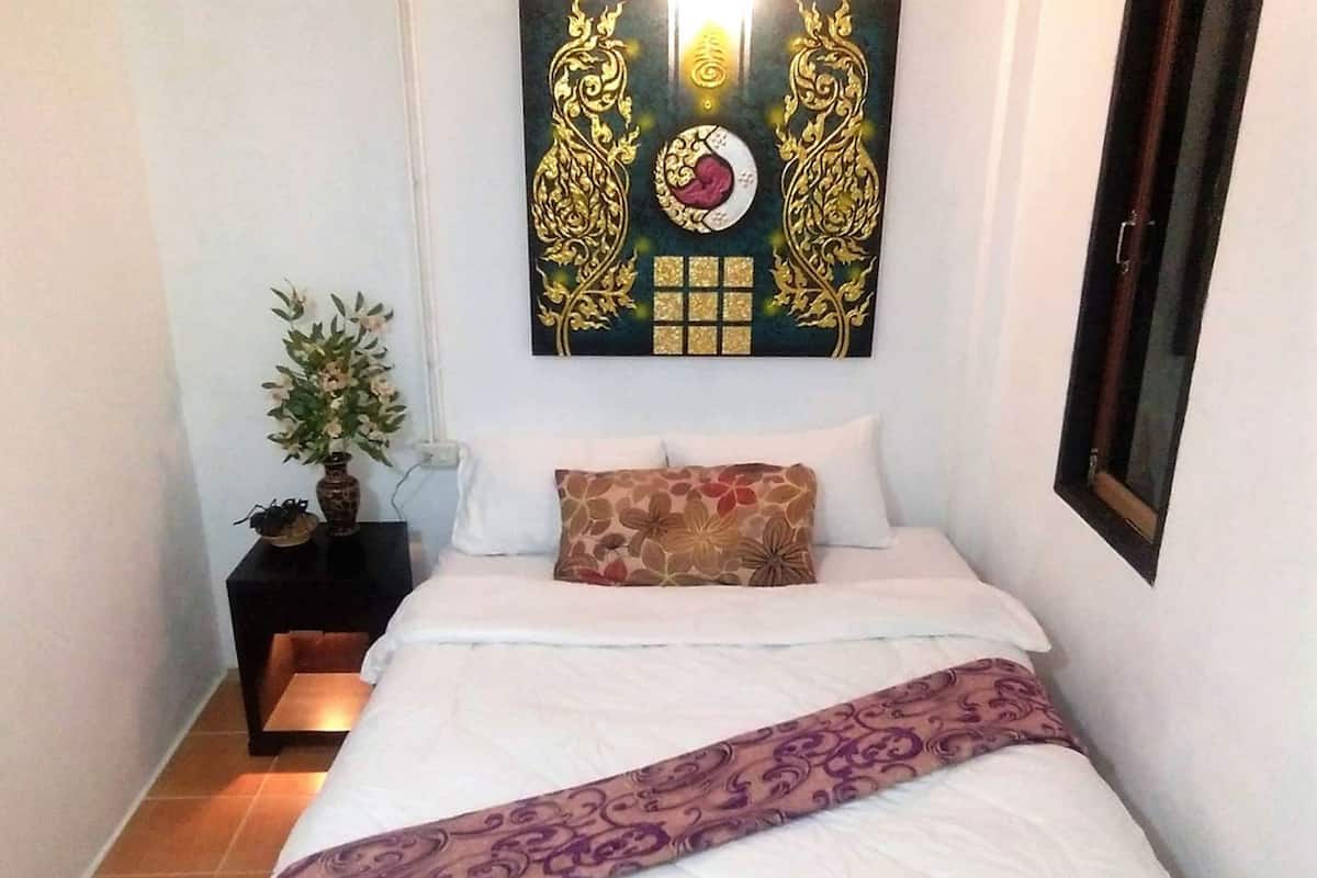Een slaapkamer met een bed, nachtkastje, hangend kunstwerk en een potplant.