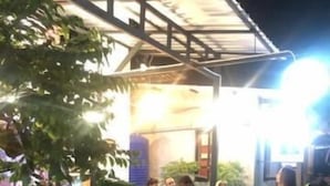 Een groep mensen zit aan tafels buiten, onder een overdekt terras met planten eromheen.