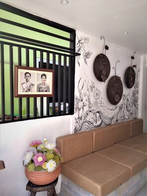 Una habitación con un sofá color crema, una fotografía enmarcada, una pared decorativa con motivos florales y de peces, y una planta en maceta con flores.