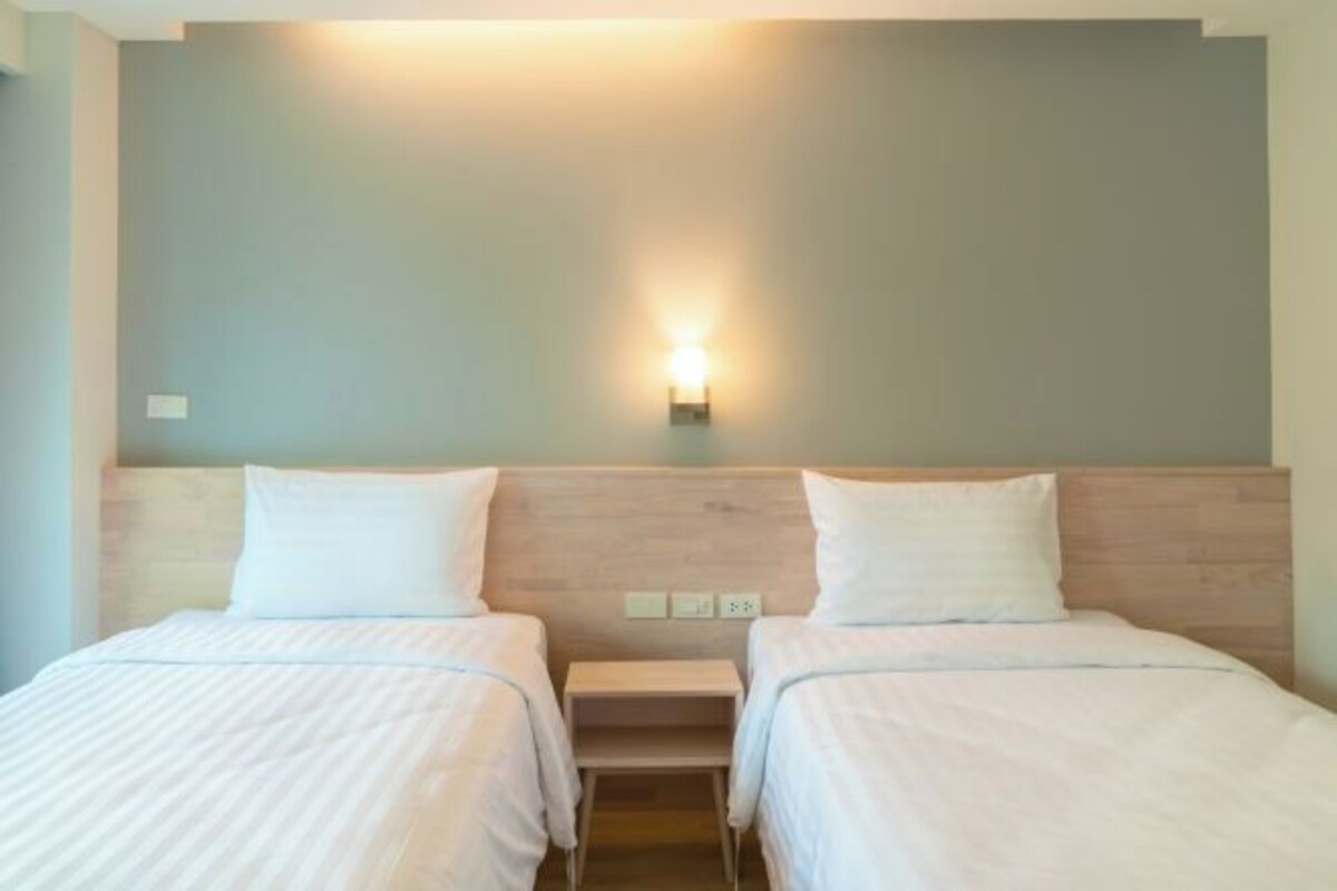 A hotel room with two beds, a nightstand, and a wall-mounted light fixture.