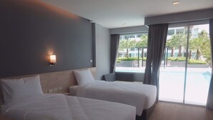 A hotel room with two beds, a nightstand, a wall-mounted lamp, and a view of a swimming pool. - Bay Window at Sea (Cha-am)