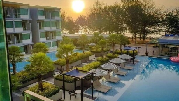 A resort with a swimming pool, sun loungers, and a view of the sunset. - Bay Window at Sea (Cha-am)