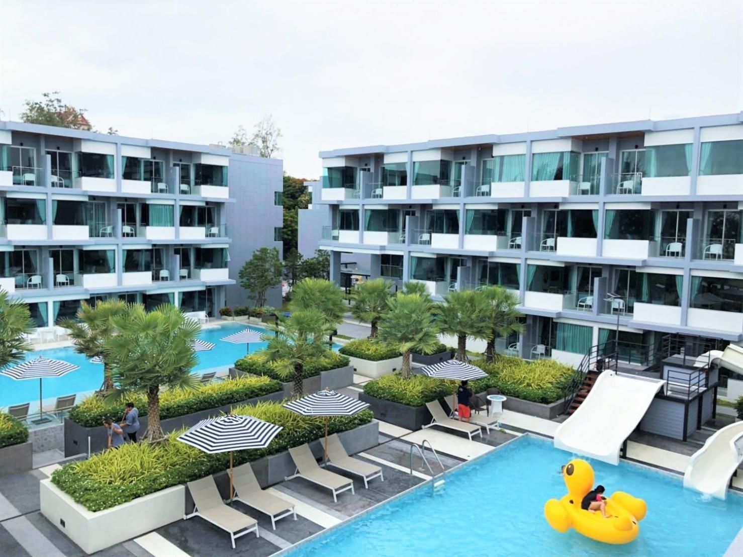 Ett modernt hotell med flera balkonger, en swimmingpool och en lekplats för barn.