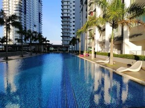 A swimming pool with tiled flooring, surrounded by palm trees and modern buildings. - Almyra Serviced Residence (Kajang)