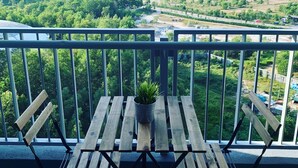 A balcony with a wooden table and chairs, a potted plant, and a view of a green landscape with buildings in the distance. - Almyra Serviced Residence (Kajang)