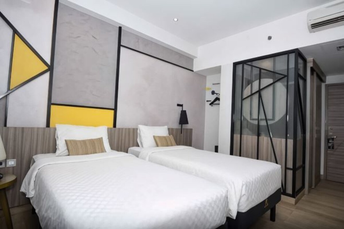 Habitación de hotel con dos camas, diseño moderno, separador de vidrio y armario visible.