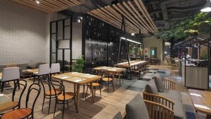 Un restaurant moderne avec des tables et des chaises en bois, un mur en briques et un plafond avec des poutres apparentes.