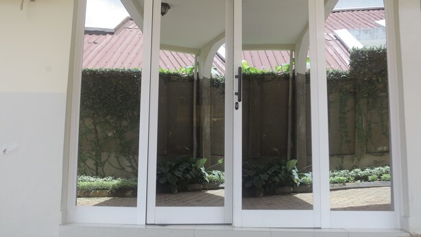 A set of white sliding glass doors leading to a covered outdoor area with a tiled floor and potted plants. - Les Flamants Rose - Gulfview (Yaoundé)