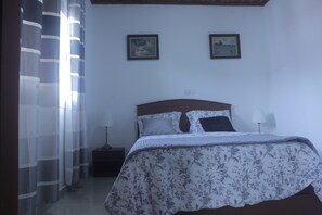 A bedroom with a bed, curtains, a nightstand, and two wall-mounted pictures.