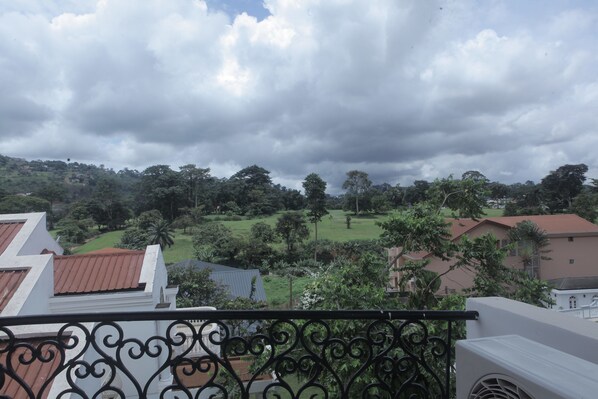 A balcony with a wrought iron railing overlooking a residential area with houses and greenery.