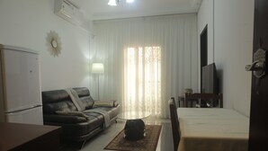 A room with a sofa, a small round table, a bed, a TV, and a window with curtains. - Les Flamants Rose - Gulfview (Yaoundé)